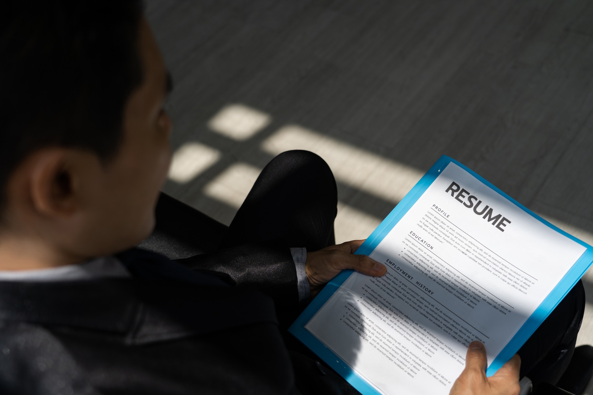 A asian young businessman man wears a black suit sitting in a chair with self-introduction documents for applying for a job. Waiting for the staff to call for a job interview in the morning.